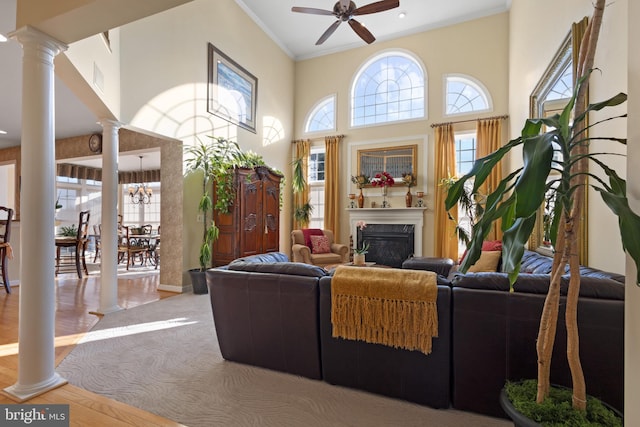 living room featuring a high ceiling, ceiling fan with notable chandelier, light hardwood / wood-style flooring, ornate columns, and ornamental molding