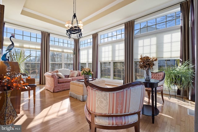 sunroom featuring a chandelier, a raised ceiling, and a wealth of natural light