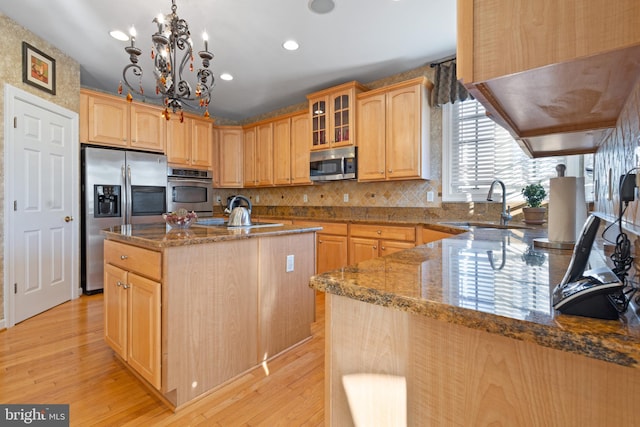 kitchen featuring dark stone counters, an inviting chandelier, a center island with sink, light hardwood / wood-style floors, and stainless steel appliances