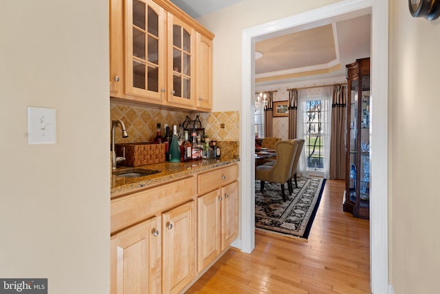 bar featuring light brown cabinetry, light stone counters, crown molding, sink, and light hardwood / wood-style flooring