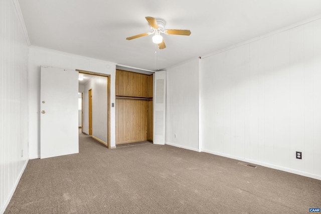 unfurnished bedroom with carpet, wood walls, ceiling fan, ornamental molding, and a closet