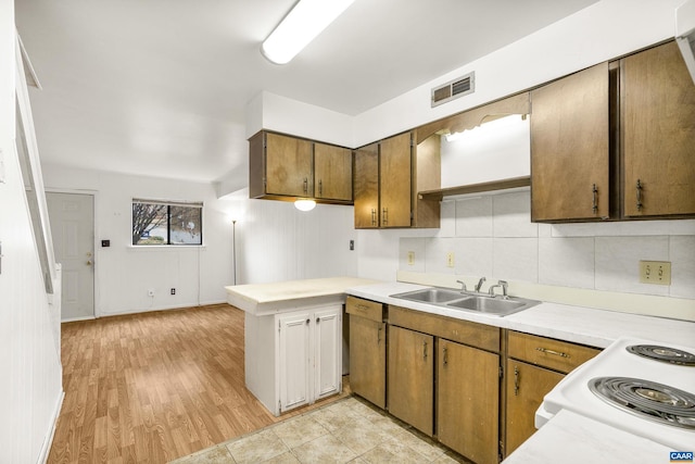 kitchen with sink, tasteful backsplash, kitchen peninsula, white stove, and light wood-type flooring