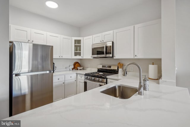 kitchen with light stone countertops, stainless steel appliances, white cabinets, and sink