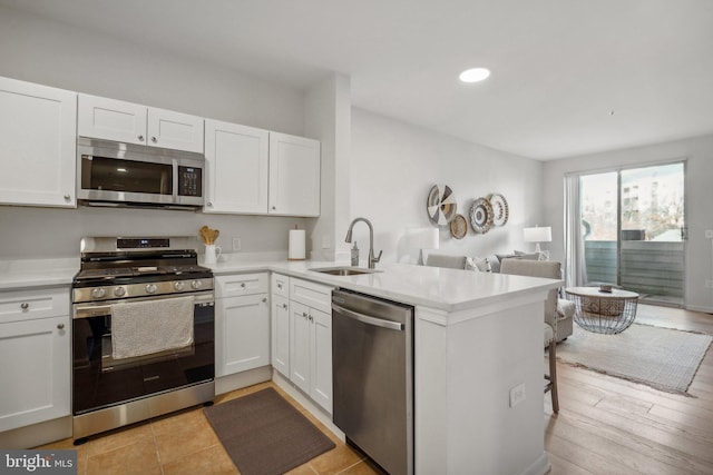 kitchen with kitchen peninsula, appliances with stainless steel finishes, white cabinets, and sink