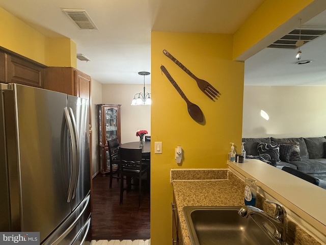 kitchen with dark hardwood / wood-style flooring, sink, pendant lighting, a notable chandelier, and stainless steel refrigerator