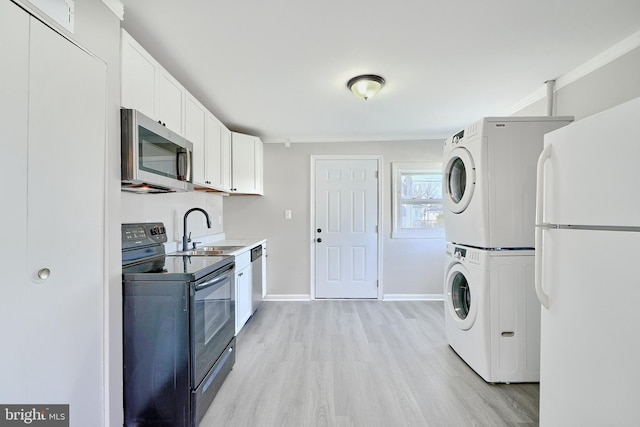 kitchen with white cabinets, sink, light hardwood / wood-style flooring, appliances with stainless steel finishes, and stacked washer / dryer