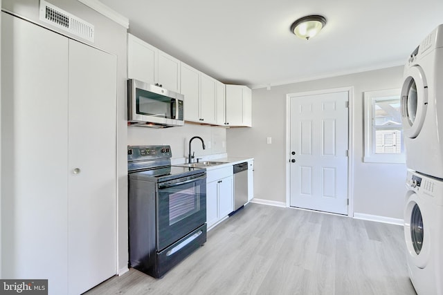 kitchen featuring sink, light hardwood / wood-style flooring, appliances with stainless steel finishes, stacked washer / drying machine, and white cabinetry