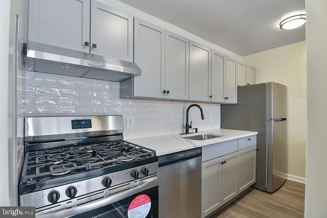 kitchen with backsplash, sink, light stone countertops, light wood-type flooring, and appliances with stainless steel finishes