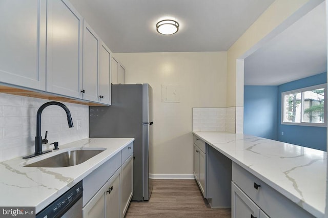 kitchen featuring light stone countertops, sink, stainless steel appliances, decorative backsplash, and light wood-type flooring