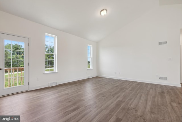 unfurnished room featuring a wealth of natural light, vaulted ceiling, and hardwood / wood-style flooring