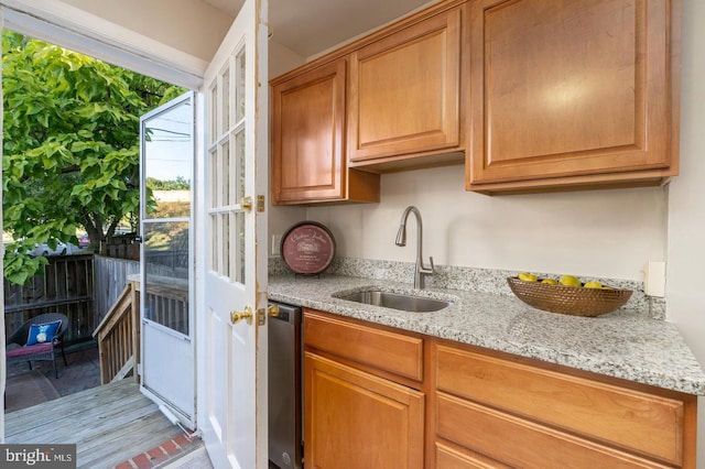 kitchen with light stone counters, sink, stainless steel dishwasher, and light hardwood / wood-style flooring