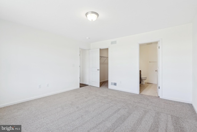 unfurnished bedroom featuring ensuite bathroom, light colored carpet, a spacious closet, and a closet