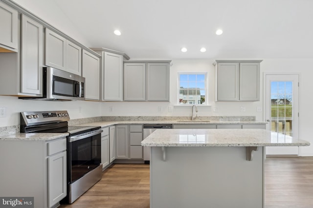 kitchen with sink, gray cabinets, light wood-type flooring, a kitchen island, and stainless steel appliances