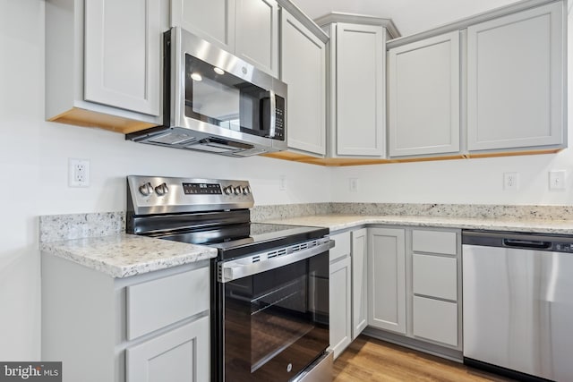 kitchen featuring light stone countertops, stainless steel appliances, and light wood-type flooring