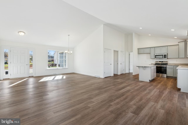 unfurnished living room with high vaulted ceiling, dark hardwood / wood-style floors, and an inviting chandelier