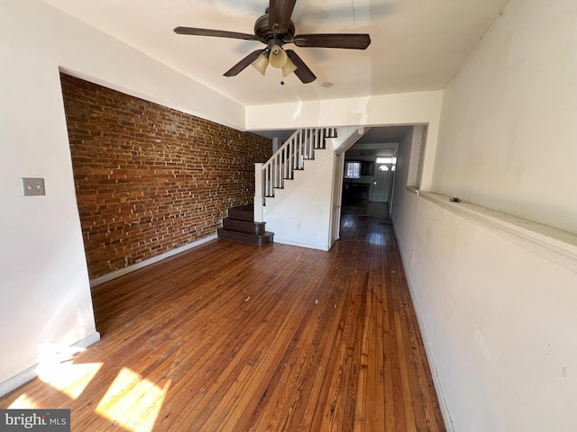 unfurnished living room with brick wall, wood-type flooring, stairway, and ceiling fan