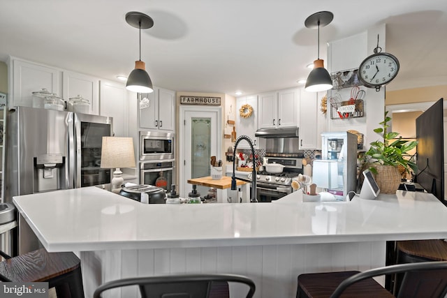 kitchen featuring white cabinetry, hanging light fixtures, stainless steel appliances, decorative backsplash, and a breakfast bar