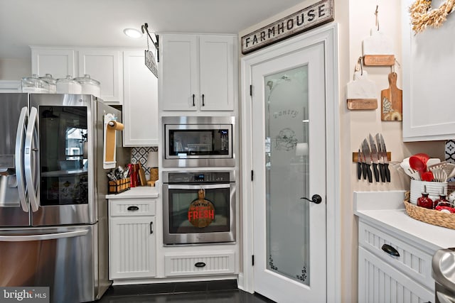 kitchen with appliances with stainless steel finishes, white cabinetry, and dark tile patterned flooring