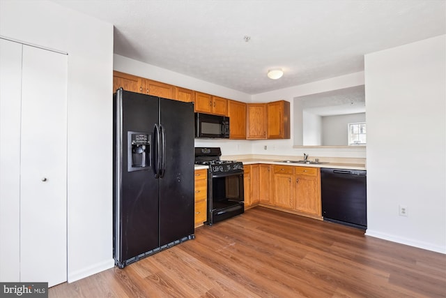 kitchen with black appliances, light wood-type flooring, a textured ceiling, and sink