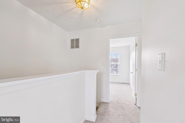 hallway with a textured ceiling and light carpet