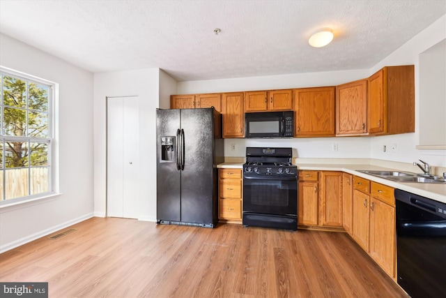 kitchen featuring a textured ceiling, light hardwood / wood-style floors, black appliances, and sink