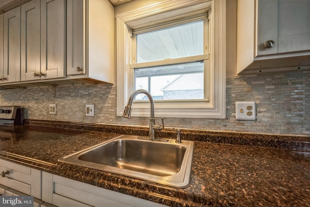 kitchen featuring backsplash, dark stone countertops, sink, and gray cabinets