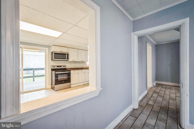 kitchen with decorative backsplash, a drop ceiling, ornamental molding, stainless steel appliances, and white cabinets