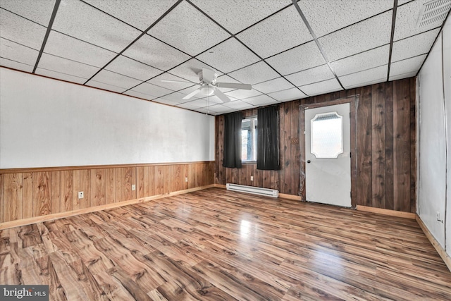 empty room with hardwood / wood-style floors, a paneled ceiling, wooden walls, and a baseboard heating unit