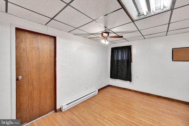 empty room featuring a drop ceiling, light hardwood / wood-style flooring, ceiling fan, a baseboard radiator, and brick wall