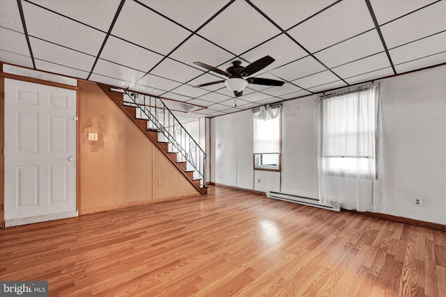 basement with light wood-type flooring, a baseboard radiator, a drop ceiling, and ceiling fan