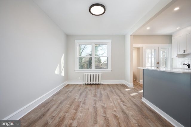 unfurnished living room with radiator heating unit, sink, and light hardwood / wood-style flooring