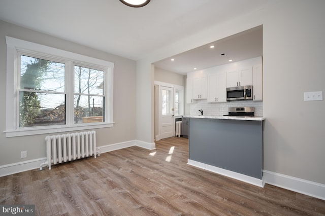 kitchen with white cabinets, radiator heating unit, stainless steel appliances, and a wealth of natural light