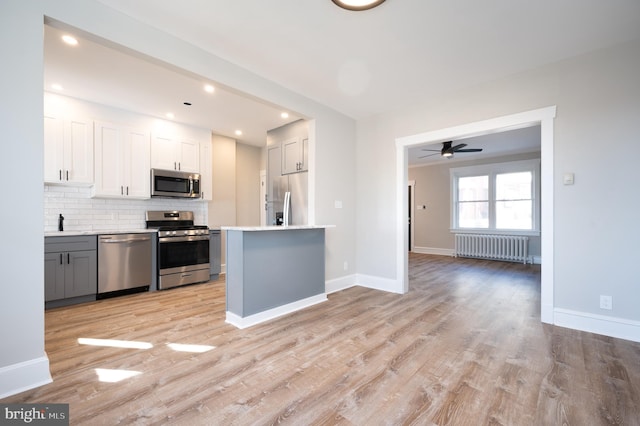 kitchen featuring gray cabinetry, white cabinets, appliances with stainless steel finishes, light hardwood / wood-style floors, and radiator heating unit