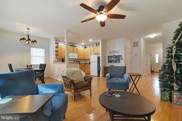 living room featuring ceiling fan with notable chandelier and light hardwood / wood-style flooring