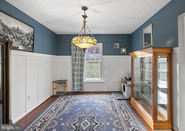 unfurnished dining area with a textured ceiling and dark wood-type flooring