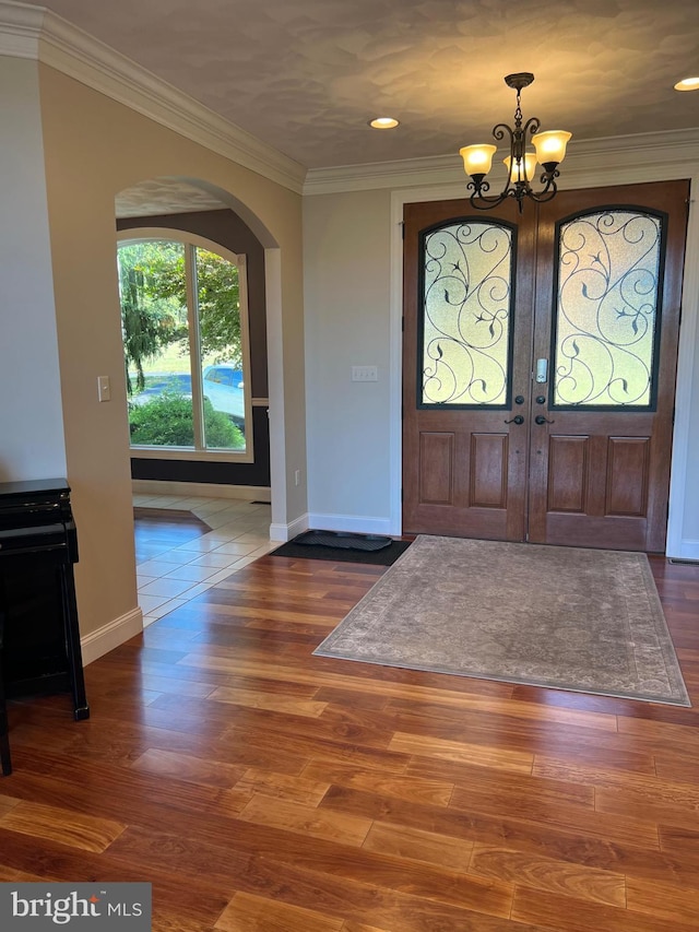 entrance foyer with dark wood-style floors, ornamental molding, arched walkways, and an inviting chandelier