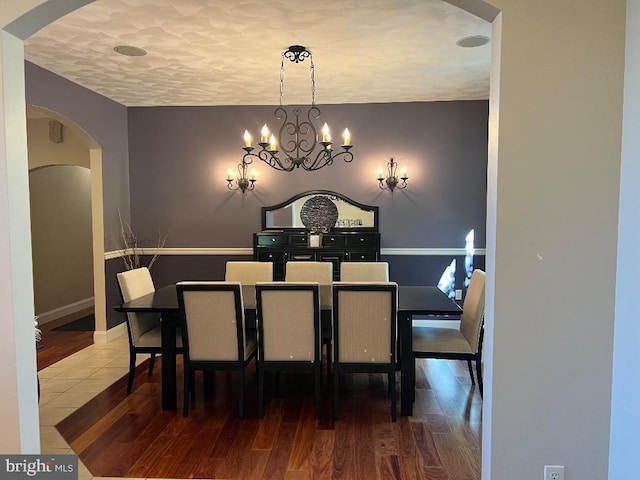 dining area with arched walkways, a textured ceiling, a notable chandelier, wood finished floors, and baseboards