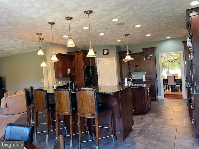 kitchen featuring open floor plan, dark stone countertops, a kitchen bar, pendant lighting, and black fridge