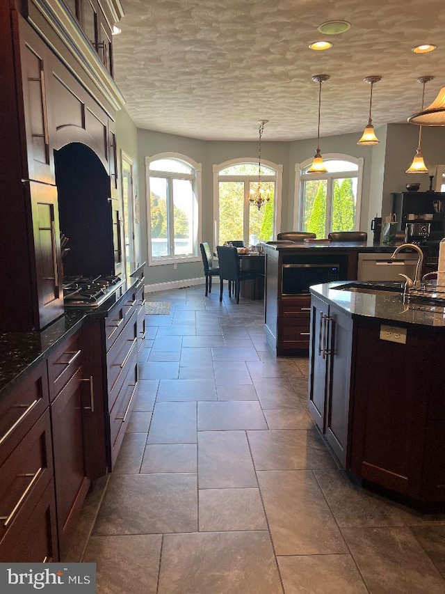 kitchen featuring a sink, baseboards, dark brown cabinets, dark stone counters, and pendant lighting