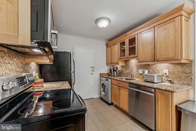 kitchen with light stone countertops, sink, washer / dryer, light tile patterned flooring, and appliances with stainless steel finishes