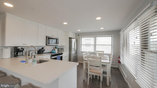 kitchen with kitchen peninsula, appliances with stainless steel finishes, dark wood-type flooring, sink, and white cabinets