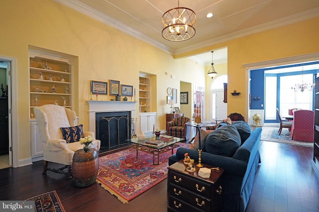 living room featuring built in shelves, dark hardwood / wood-style flooring, ornamental molding, and a chandelier