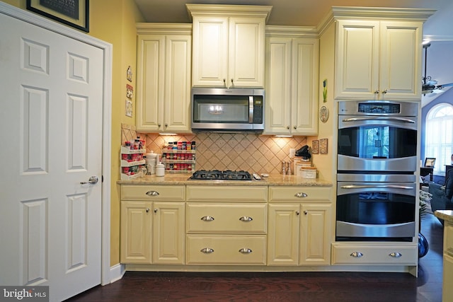 kitchen featuring backsplash, light stone countertops, stainless steel appliances, and cream cabinetry