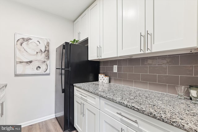 kitchen featuring white cabinetry, black fridge, light stone counters, backsplash, and light hardwood / wood-style floors