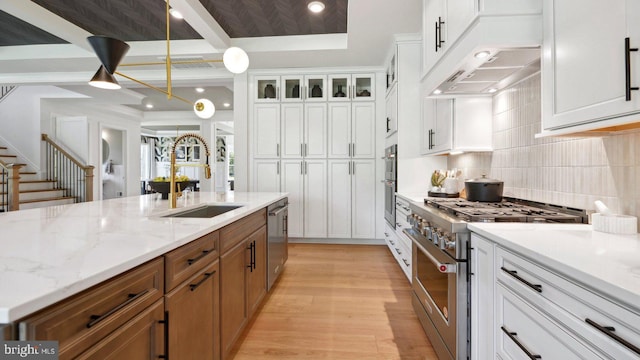 kitchen with light stone countertops, appliances with stainless steel finishes, light wood-type flooring, sink, and white cabinetry