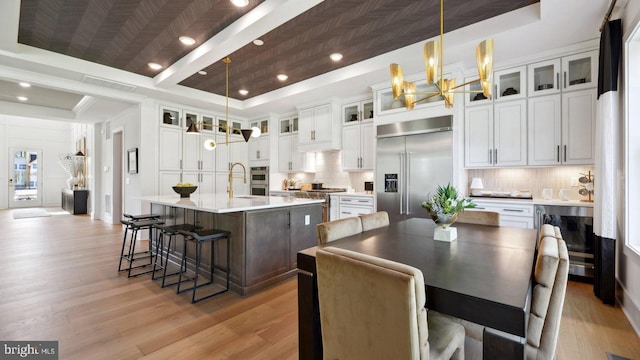 kitchen with a center island with sink, pendant lighting, stainless steel built in refrigerator, and a tray ceiling