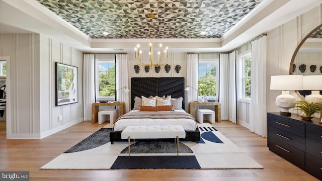 bedroom with a raised ceiling, light wood-type flooring, and a chandelier