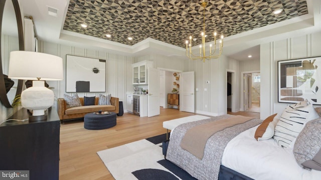 bedroom featuring light wood-type flooring, a raised ceiling, beverage cooler, and a notable chandelier