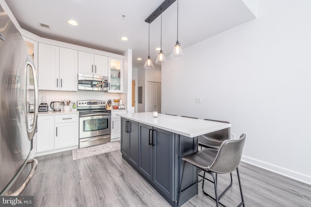 kitchen featuring light hardwood / wood-style flooring, backsplash, decorative light fixtures, white cabinets, and appliances with stainless steel finishes