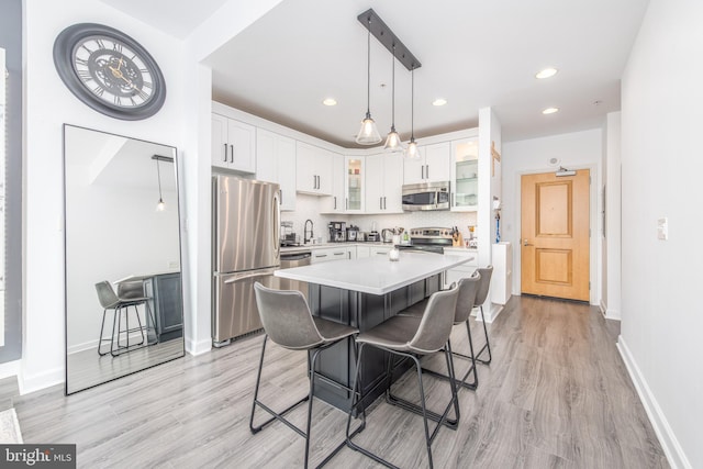 kitchen with light wood-type flooring, appliances with stainless steel finishes, a kitchen island, a kitchen bar, and white cabinetry